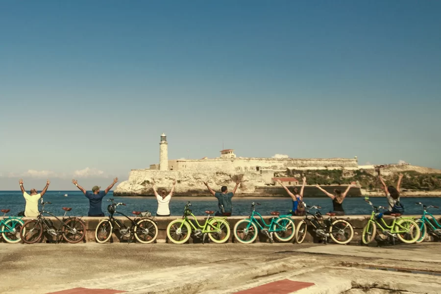 Small group on bicycles along the coast, view of the sea and historic lighthouse in the harbour of Havana, Cuba